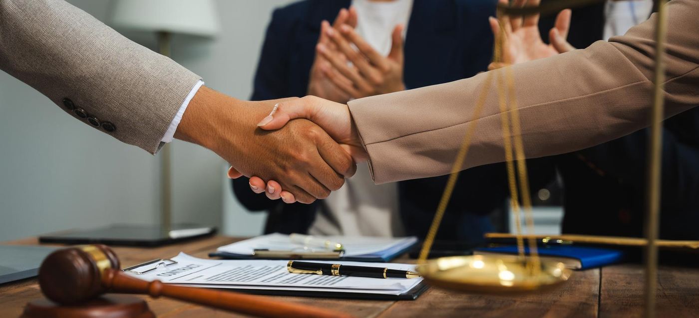 Two professionals shaking hands over a desk bearing a gavel and scales of justice